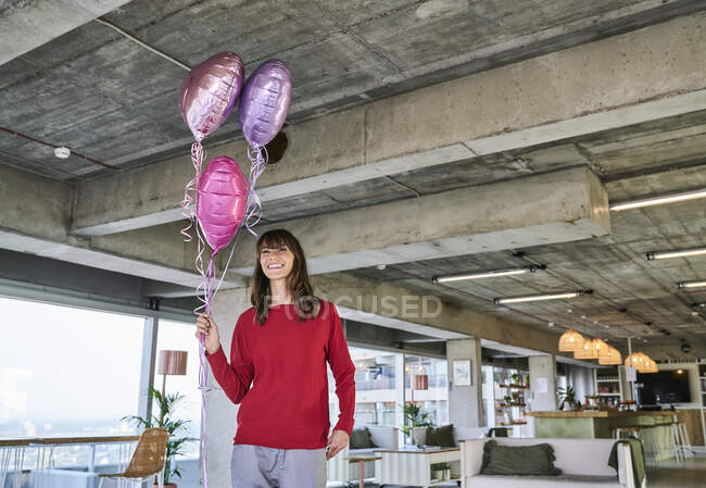 Businesswoman holding balloons while standing in loft office — Stock Photo