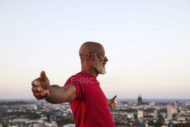 Happy completely bald man standing with arms outstretched on building terrace in city during sunset — Stock Photo