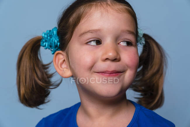 Fille souriante avec regard latéral debout sur fond bleu — Photo de stock
