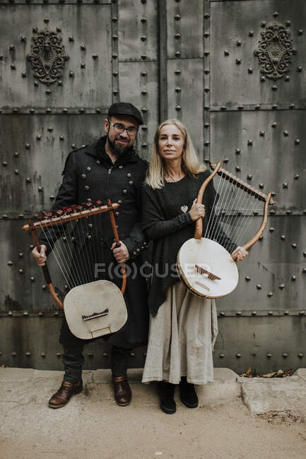 Male and female couple holding lyra musical instrument against metallic door — Stock Photo