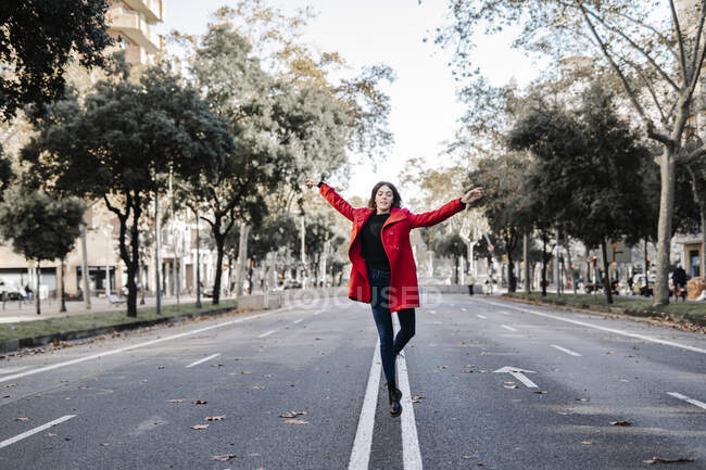 Безтурботна жінка в червоній куртці танцює під час стрибків на вулиці — стокове фото