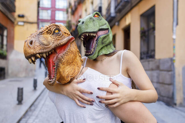 Hombre dando paseo a caballo a hembra en máscara de dinosaurio en la ciudad - foto de stock