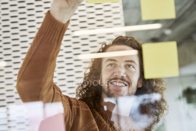 Lächelnder Mann klebt zu Hause Klebezettel auf Glasmaterial — Stockfoto