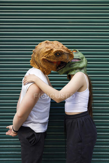 Hombre y mujer en máscara de dinosaurio besándose contra obturador verde - foto de stock