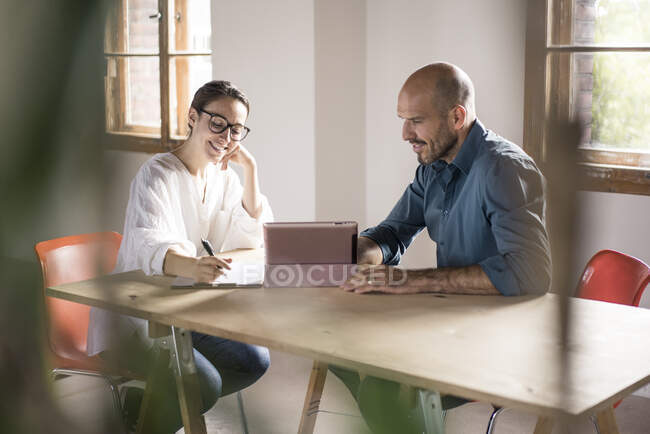 Бизнесвумен пишет в блокноте, сидя на мужчине, используя цифровой планшет в офисе — стоковое фото