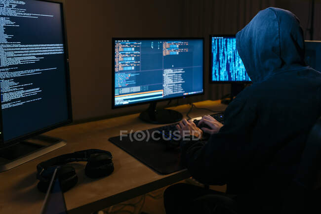 Hacker wearing hoodie working on computer while sitting at office — Stock Photo