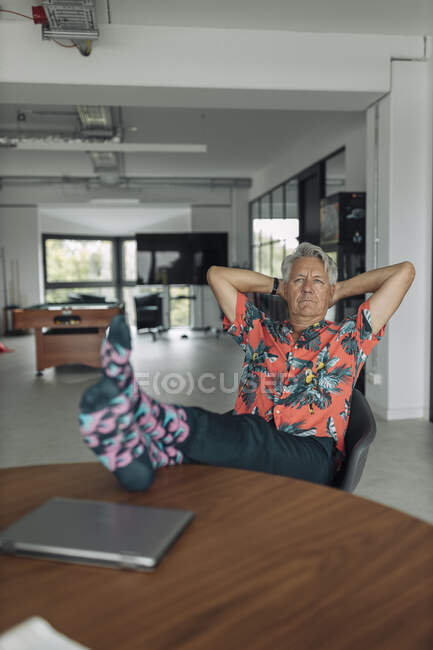 Бизнесмен с руками за головой сидит со скрещенными ногами на столе в офисе — стоковое фото