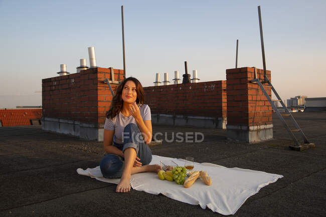 Jeune femme réfléchie ayant des fruits pendant le pique-nique sur le toit — Photo de stock