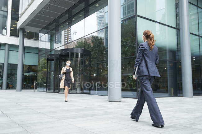 Empresários usando máscara facial enquanto caminham contra prédio de escritórios — Fotografia de Stock