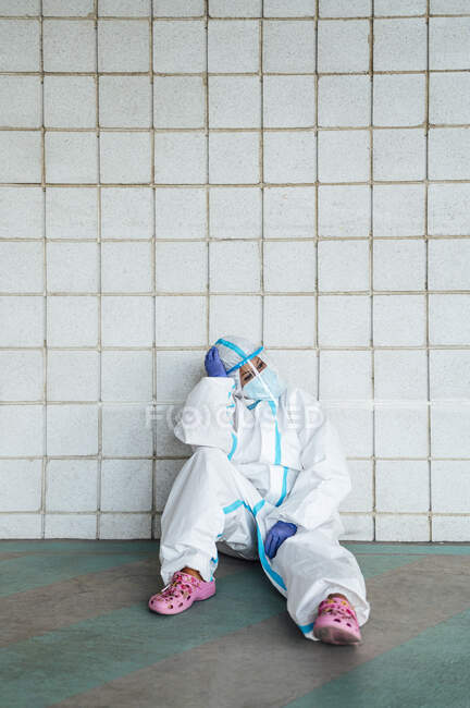 Созерцая медсестру с головой в руках, сидящую напротив плитки стены — стоковое фото