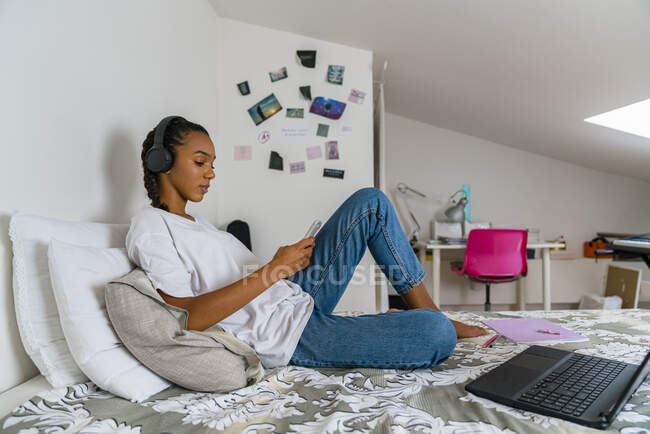 Молода дівчина слухає музику, використовуючи смартфон, сидячи вдома в спальні — стокове фото