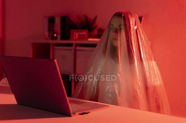Worried woman covered in plastic sitting with laptop at desk in home office during coronavirus crisis — Stock Photo