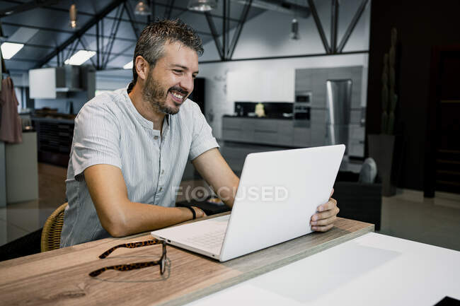 Улыбающийся мужчина-профессионал смотрит на ноутбук, выполняя внештатную работу в офисе — стоковое фото