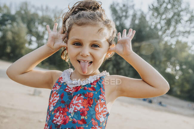 Menina bonito saindo da língua enquanto está de pé na praia — Fotografia de Stock