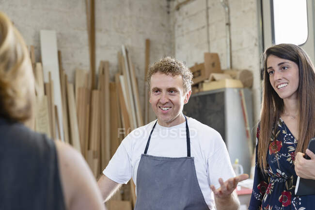 Smiling coworker and project manager talking to employee while standing at workshop — Stock Photo