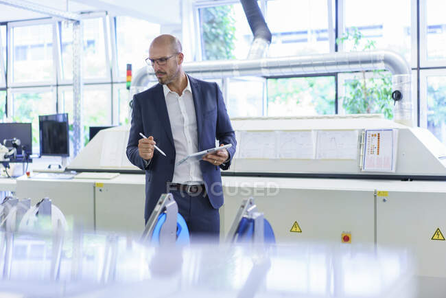 Mature male professional holding digital tablet while looking at machinery in factory — Stock Photo