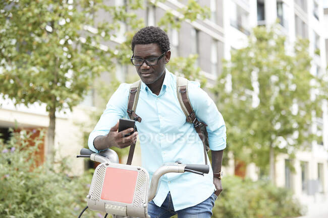Homme utilisant un téléphone intelligent tout en se tenant debout avec vélo en ville — Photo de stock