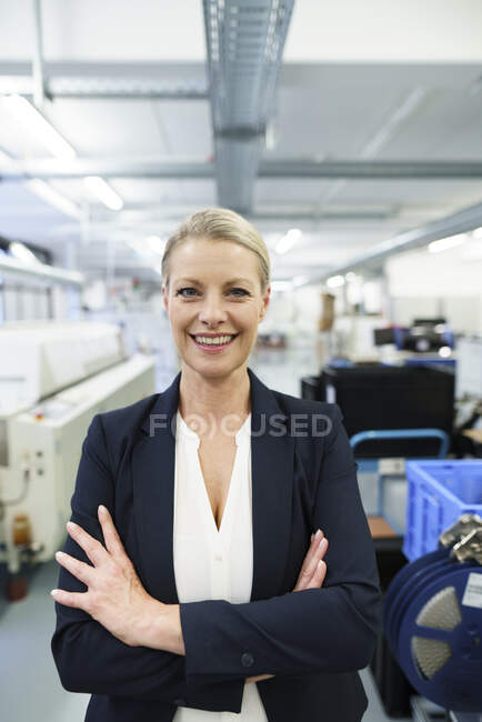 Smiling mature blond female professional standing with arms crossed at illuminated industry — Stock Photo