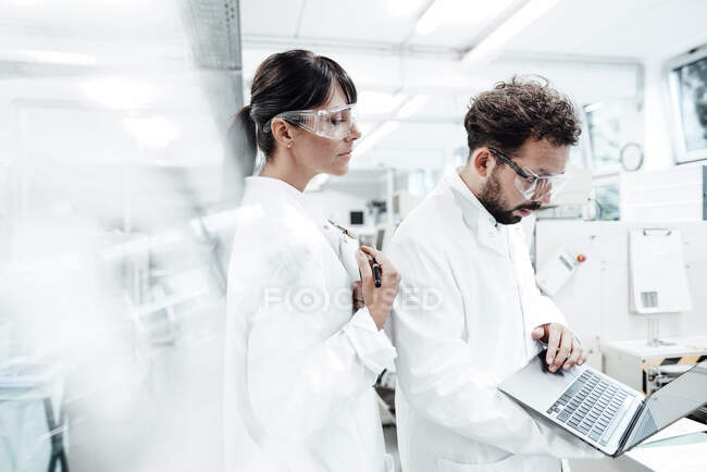 Жіночий вчений, який стоїть поруч з колегою по роботі з ноутбуком у лабораторії. — стокове фото