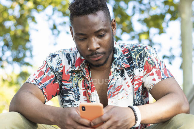 Young man using smart phone while sitting outdoors — Stock Photo
