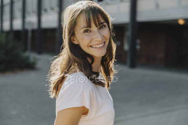 Доросла жінка посміхається, стоячи на вулиці в сонячний день. — стокове фото