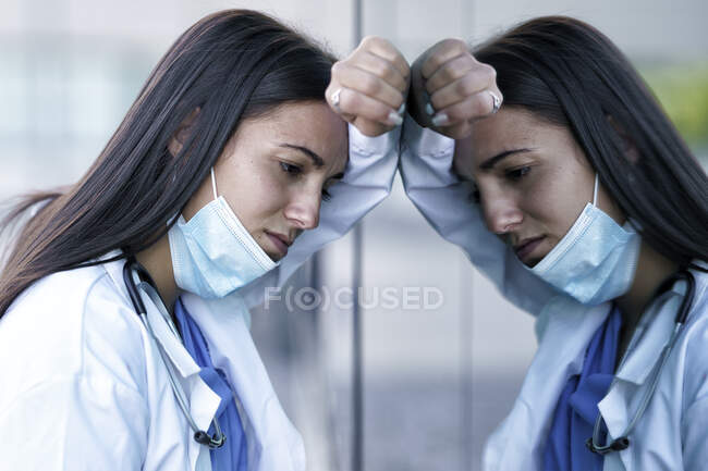 Втомлений лікар у масці на скляній стіні лікарні. — стокове фото