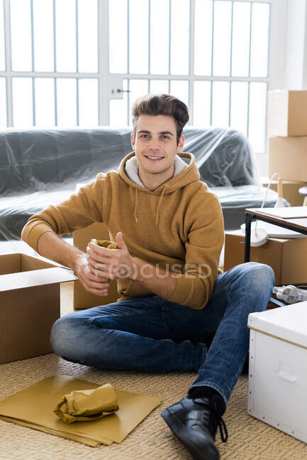 Улыбающийся человек упаковывает упакованное питьевое стекло в коробку в новой квартире — стоковое фото