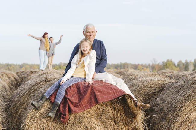 Nonno e nipote seduti su balla di fieno mentre nonna e nipote in background — Foto stock