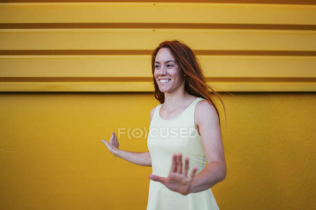 Lächelnde Frau gestikuliert, während sie vor gelber Wand steht — Stockfoto