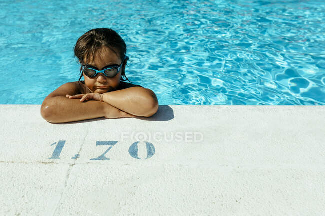 Симпатичный мальчик со скрещенными руками, склоняющийся у бассейна в солнечный день — стоковое фото