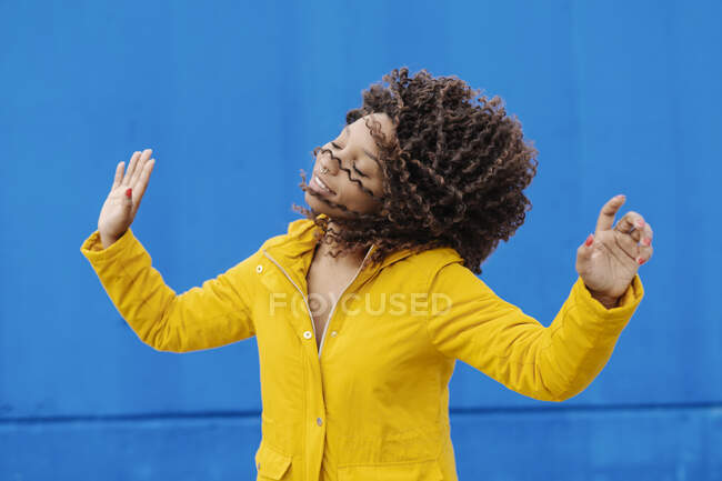 Mujer sonriente sacudiendo el pelo mientras baila contra la pared azul - foto de stock