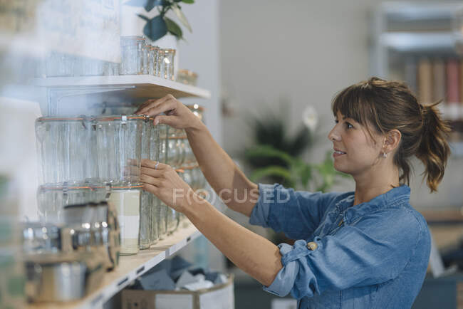 Молодая предпринимательница устраивает стеклянную банку на полке в кафе — стоковое фото