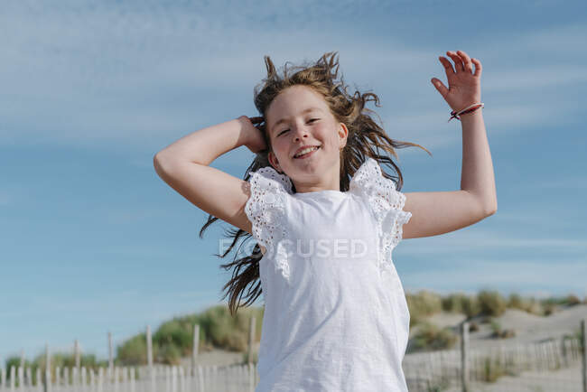 Fille avec la main dans les cheveux debout à la plage le jour ensoleillé — Photo de stock
