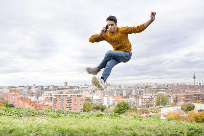 Молодий чоловік стрибає по телефону через пагорб проти міста — стокове фото
