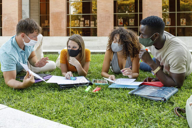 Чоловіки і жінки під час обговорення на траві в університетському містечку носять захисну маску. — стокове фото