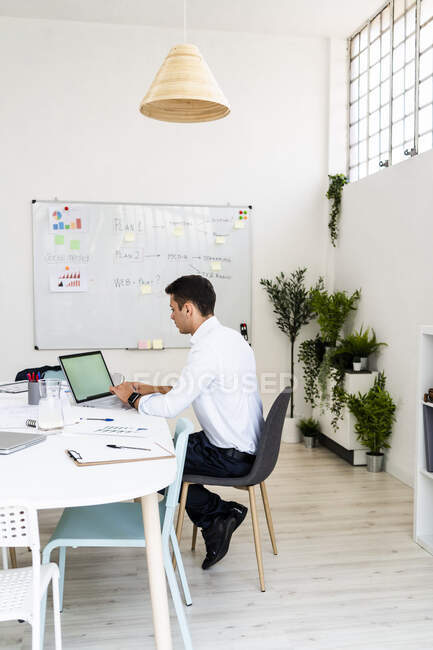 Professionista maschio utilizzando il computer portatile mentre seduto alla scrivania a lavorare sulla strategia in ufficio — Foto stock
