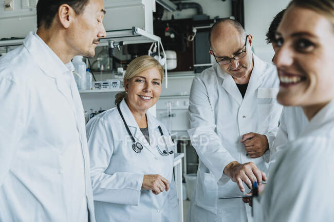 Científico sonriente trabajando junto con la tableta digital mientras está de pie en el laboratorio - foto de stock