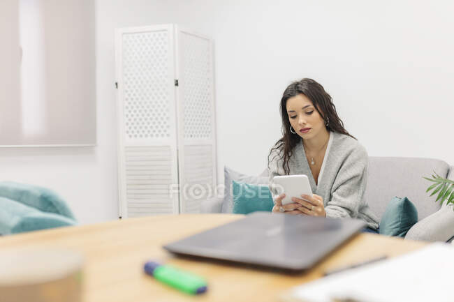Giovane donna che utilizza tablet digitale mentre seduto sul divano in ufficio — Foto stock