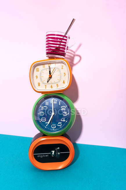 Coffee cup kept over clock stack against blue and pink background — Stock Photo