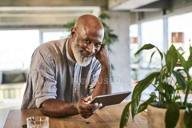 Sorrindo homem maduro segurando tablet digital enquanto se inclina na mesa no terraço da construção — Fotografia de Stock