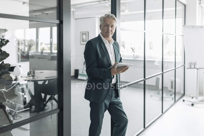 Empresário usando tablet digital enquanto se inclina na parede no escritório — Fotografia de Stock