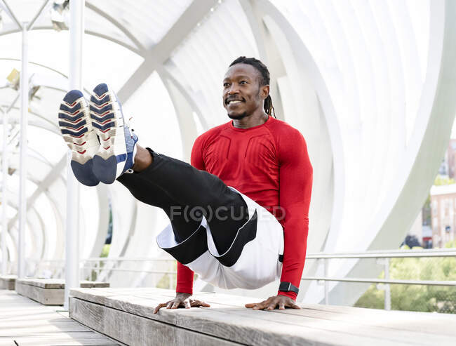 Atleta sorrindo fazendo suporte de mão no banco na passarela — Fotografia de Stock