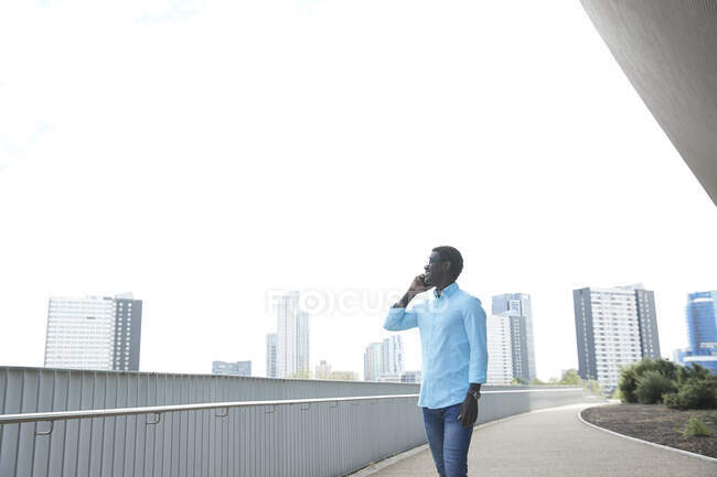 Sorrindo homem maduro olhando embora enquanto falava no telefone inteligente contra o céu limpo na cidade — Fotografia de Stock