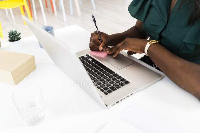 Donna d'affari che scrive sulla nota adesiva mentre lavora sul computer portatile in ufficio — Foto stock