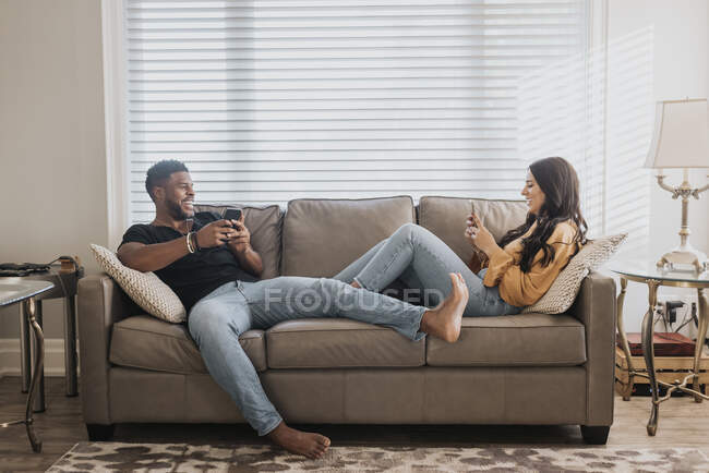 Пара використовує мобільний телефон, сидячи на дивані вдома — стокове фото