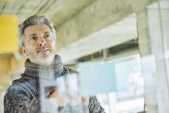 Sonriente hombre de negocios planeando mientras está de pie junto a la pared de vidrio en la oficina - foto de stock