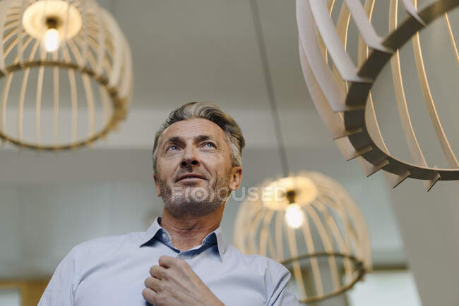 Businessman standing by illuminated light fixture at office — Stock Photo