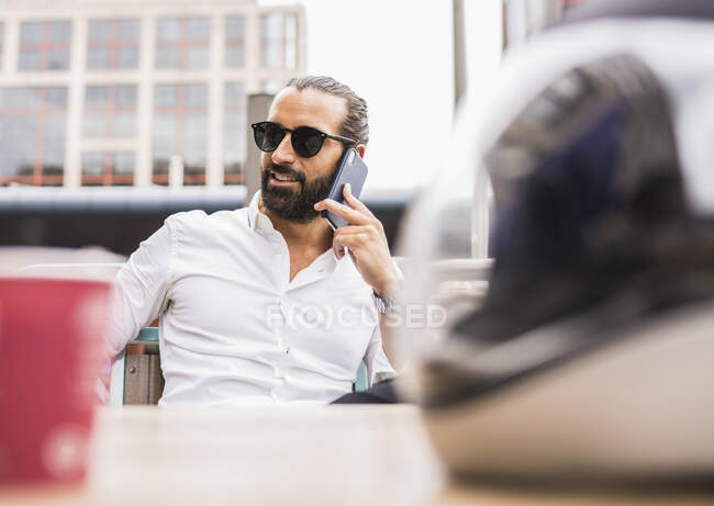 Портрет бородатого бізнесмена у сонцезахисних окулярах, який розмовляє на відкритому повітрі по смартфону. — стокове фото