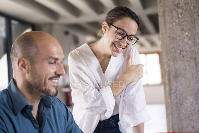 Mujer de negocios sonriente de pie por el hombre en la oficina - foto de stock