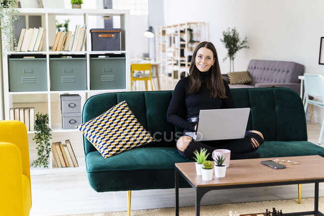 Giovane blogger seduta con computer portatile sul divano nell'appartamento soppalco — Foto stock
